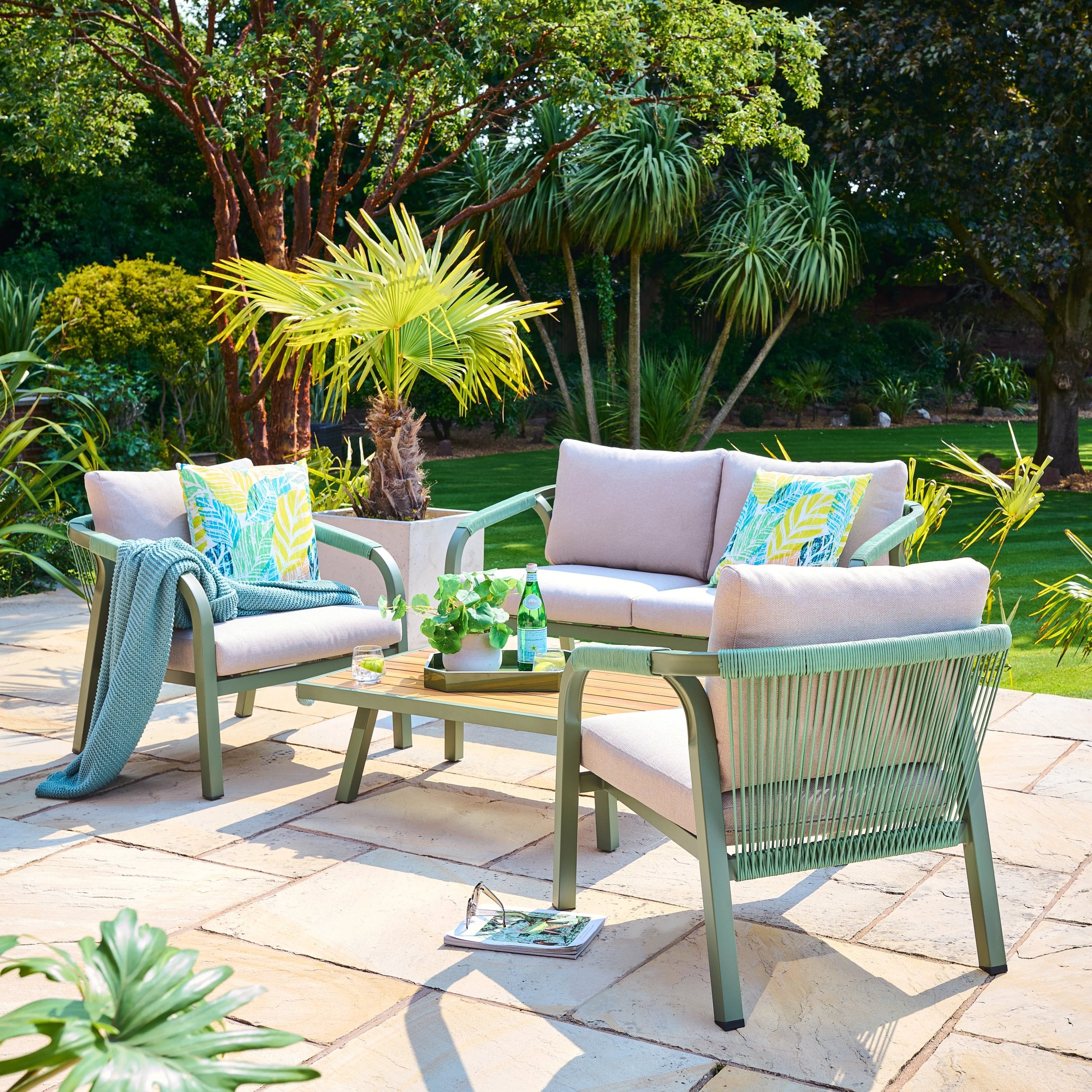 Outdoor patio set with green chairs and pink cushions in a garden setting.