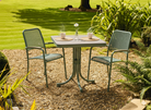 Outdoor garden table with two chairs on a gravel area with grass and plants in the background