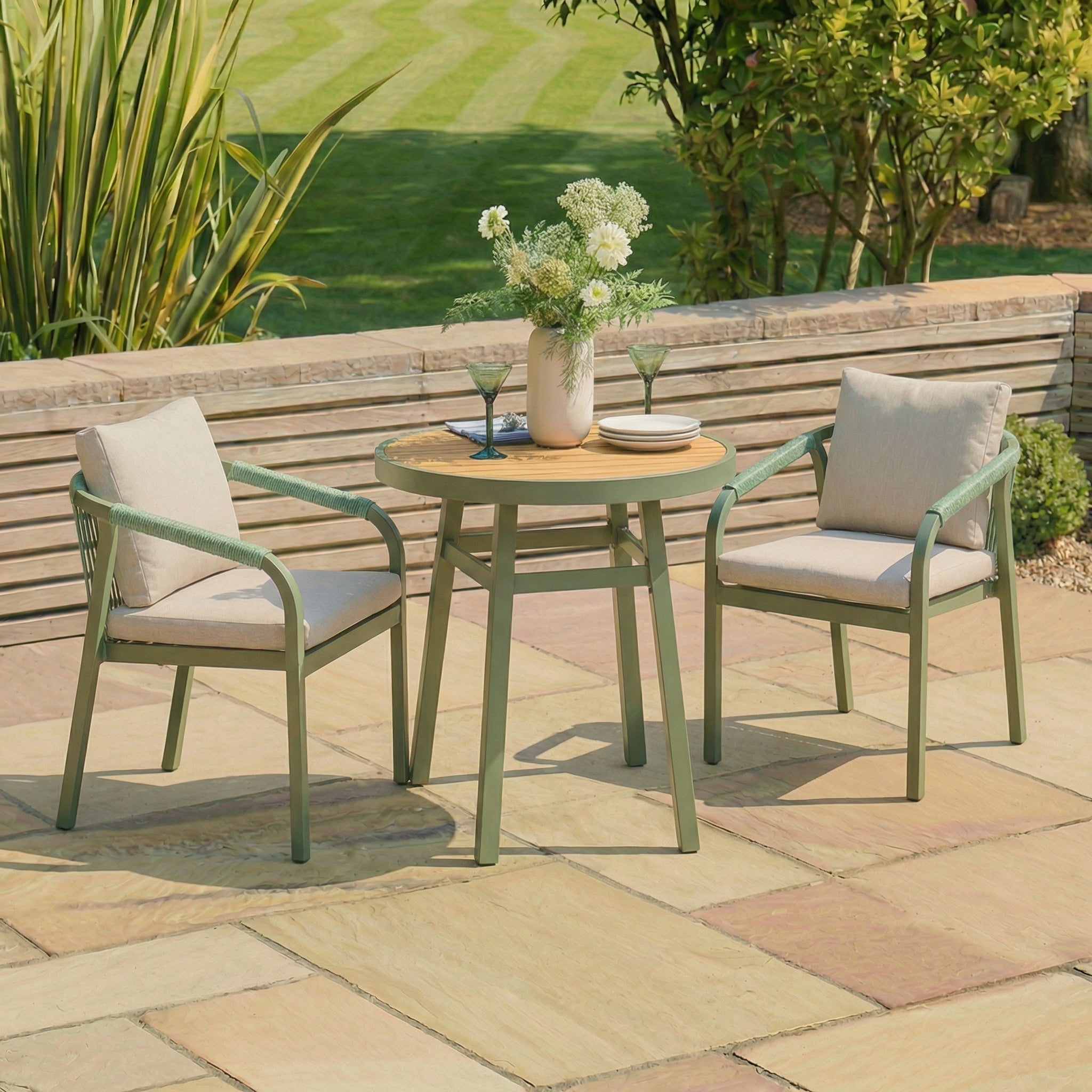 Outdoor patio set with two chairs and a table on a stone patio, surrounded by greenery.