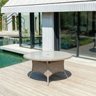 Round outdoor table on a wooden deck by a poolside house.