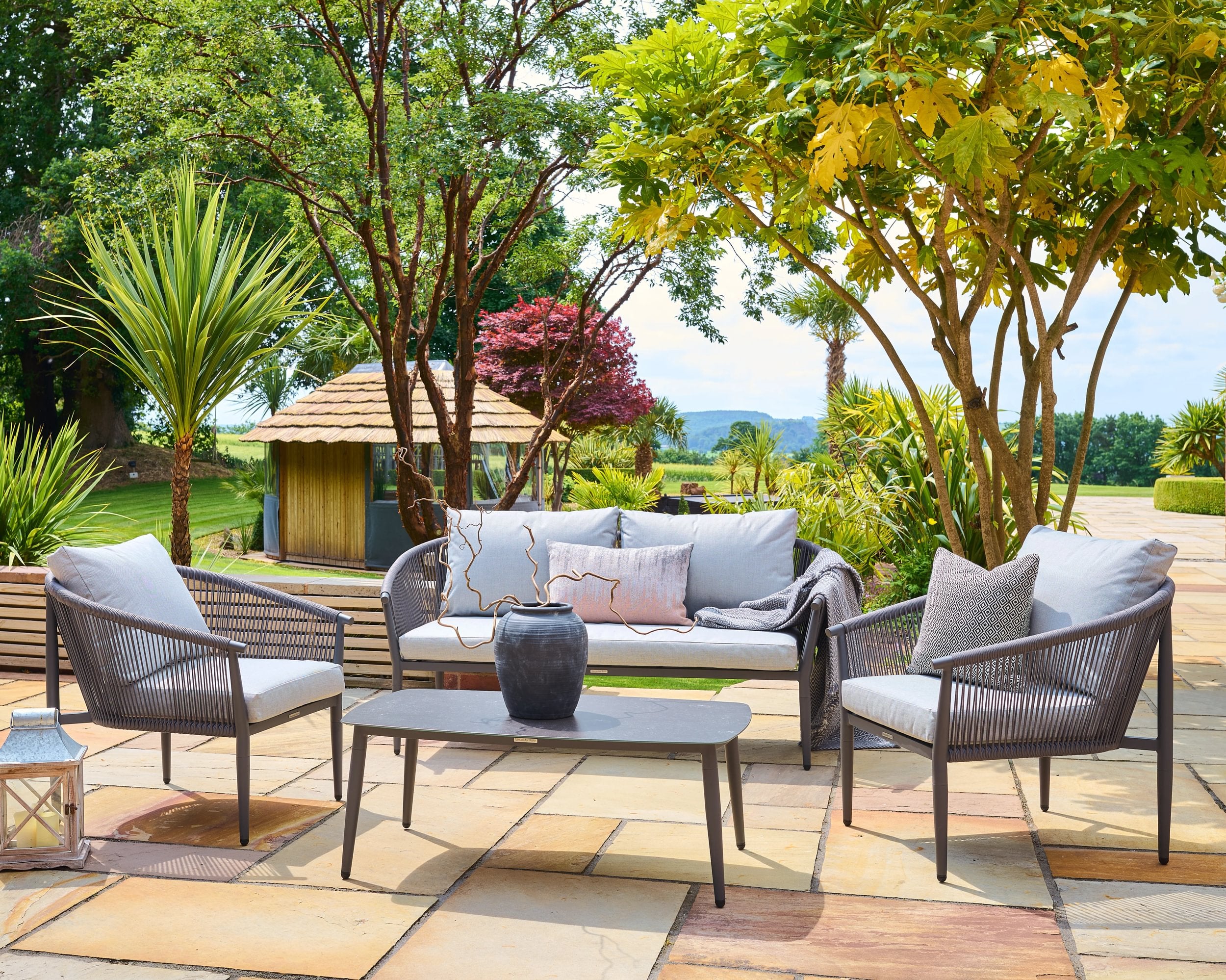 Kyoto outdoor patio set with chairs, table, and sofa on a stone patio with trees and garden in the background.