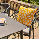 Outdoor setting with a chair featuring a yellow floral outdoor cushion and a table.