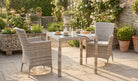 Outdoor patio set with table and chairs surrounded by flowers and plants.