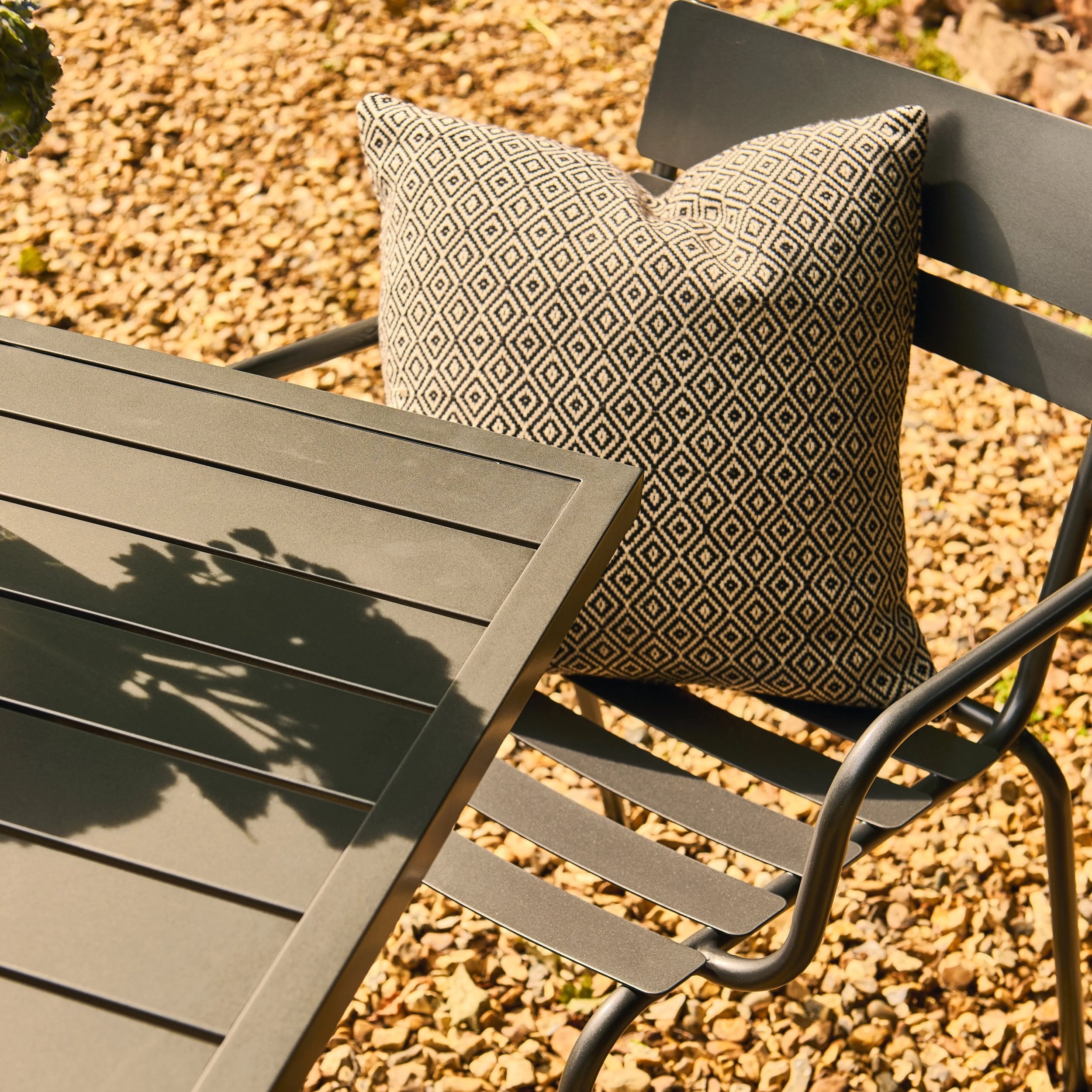 Outdoor chair with a patterned cushion next to a table on a gravel surface