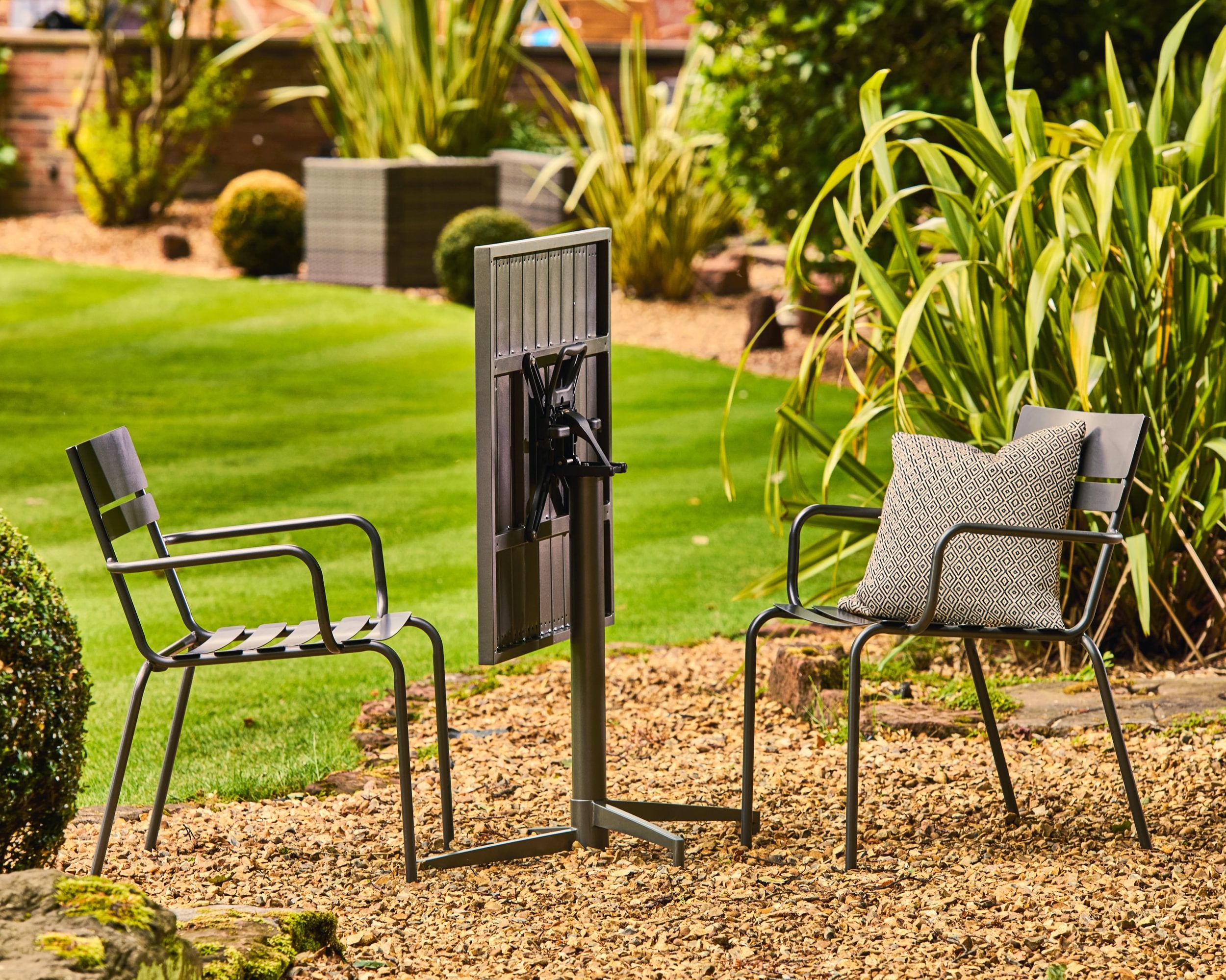 Garden scene with two chairs and a folding table in a garden setting.