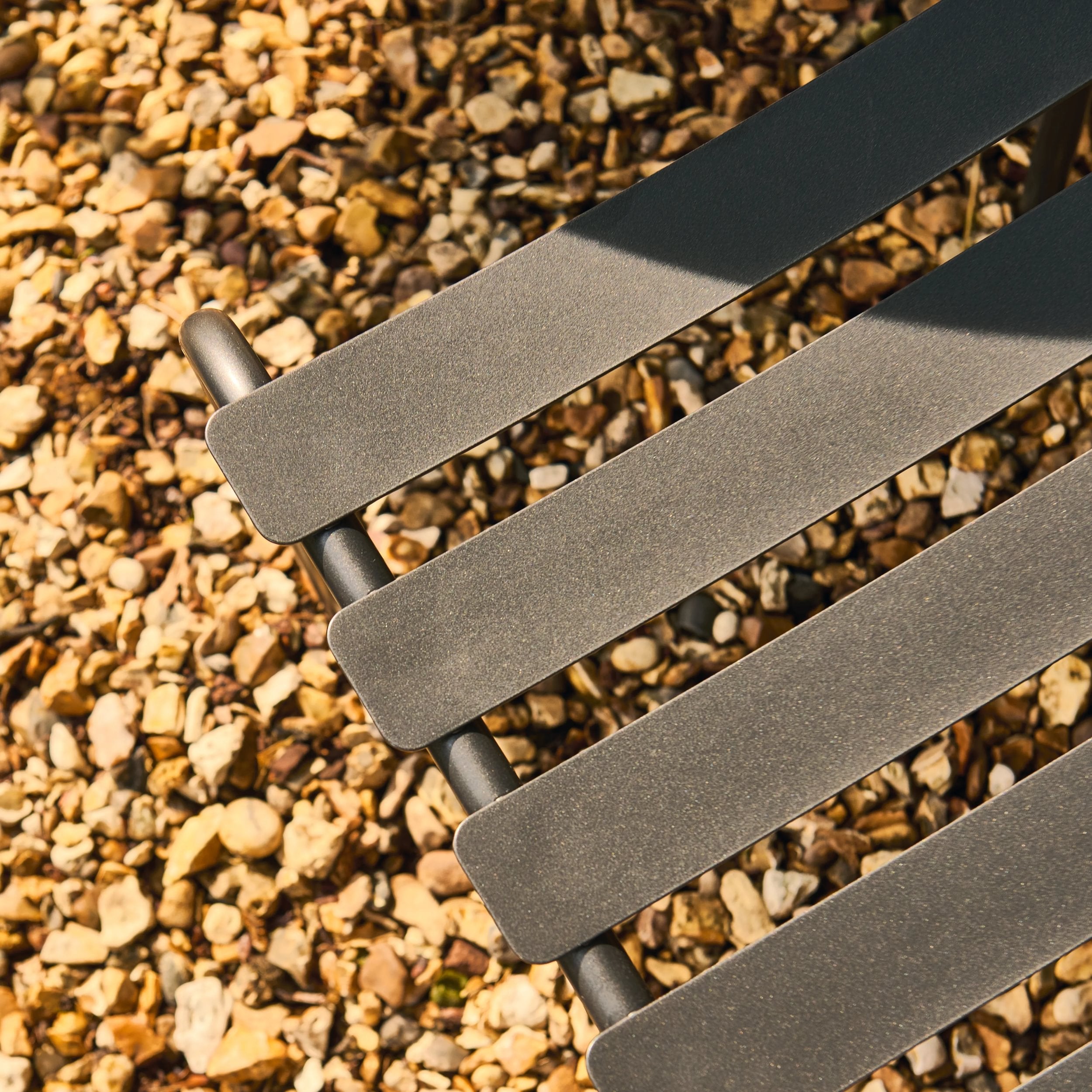 Close-up of a metal chair with slatted seat on a gravel surface