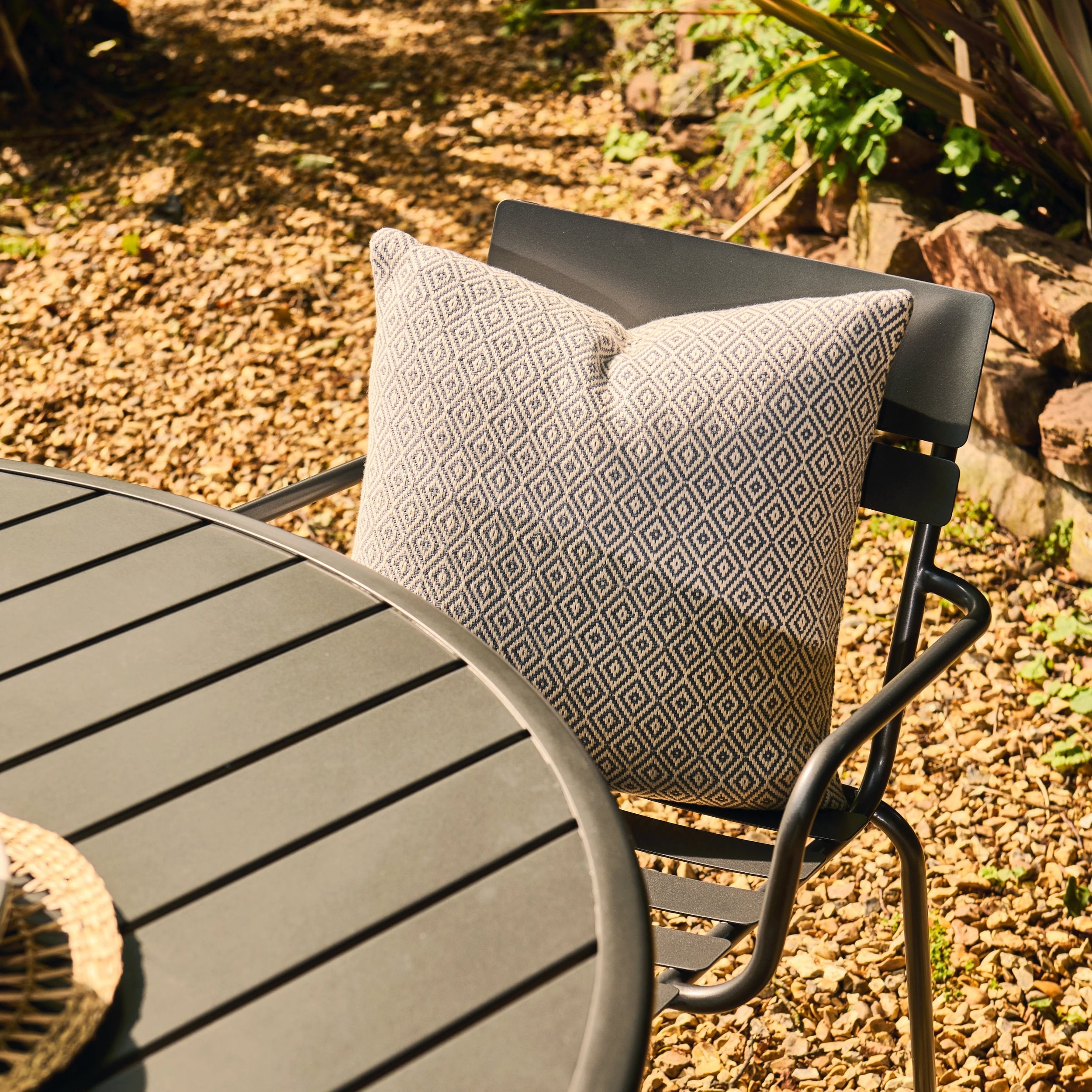 Chair with a patterned cushion on a gravel surface with plants in the background