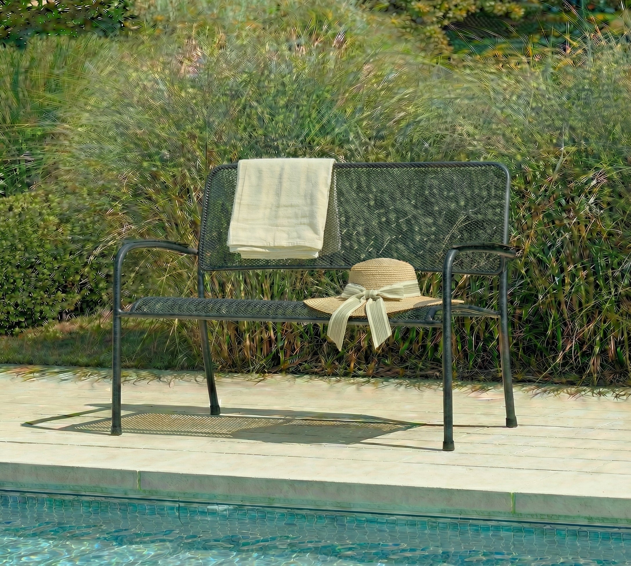 Garden bench with a towel and hat on a wooden deck by a pool