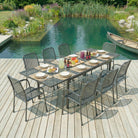 Outdoor dining setup on a wooden deck by a pond with chairs and a table.