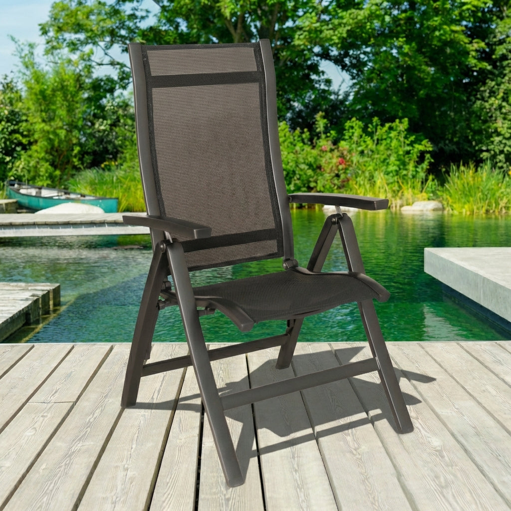 Gray outdoor reclining chair on a wooden deck by a pool with greenery in the background