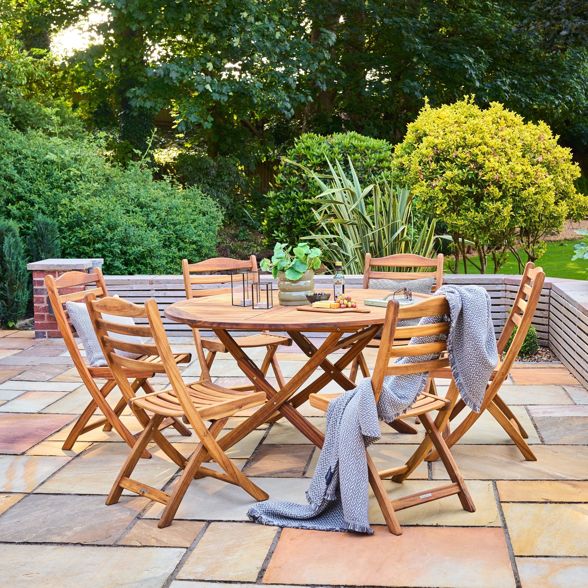 Wooden outdoor dining set with table and chairs on a patio surrounded by greenery.