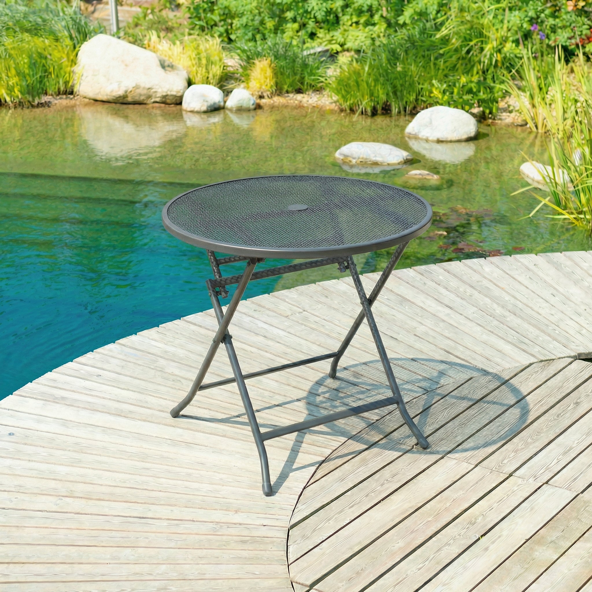 Black metal folding table on a wooden deck by a pond with greenery.