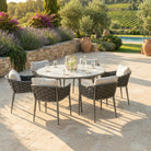 Outdoor patio set with round table and chairs on a stone patio, surrounded by garden and pool area.