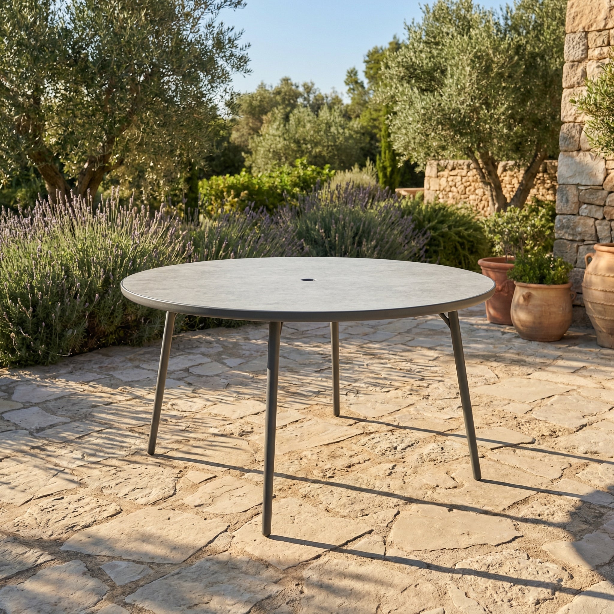 Round outdoor table on a stone patio with greenery and stone wall in the background