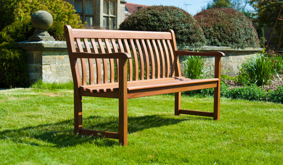Cornis Broadfield Wooden bench 5ft in a garden setting with green grass and trees.