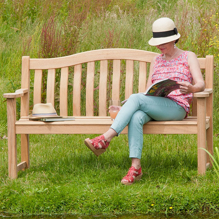 Woman sitting on a roble turnberry 5ft wooden bench in a garden reading a book.