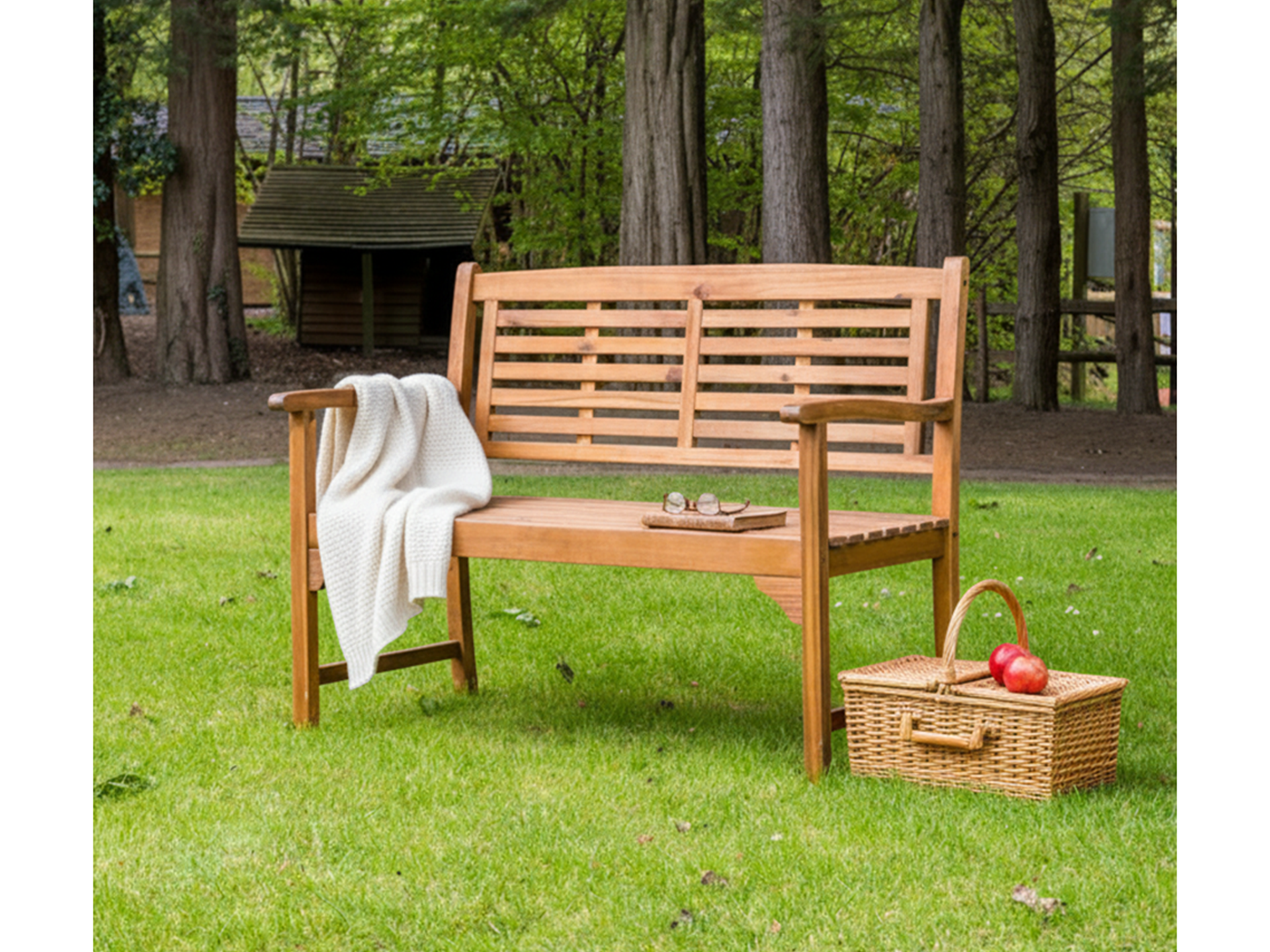 Wooden bench with a picnic basket and apples on a grassy area with trees in the background