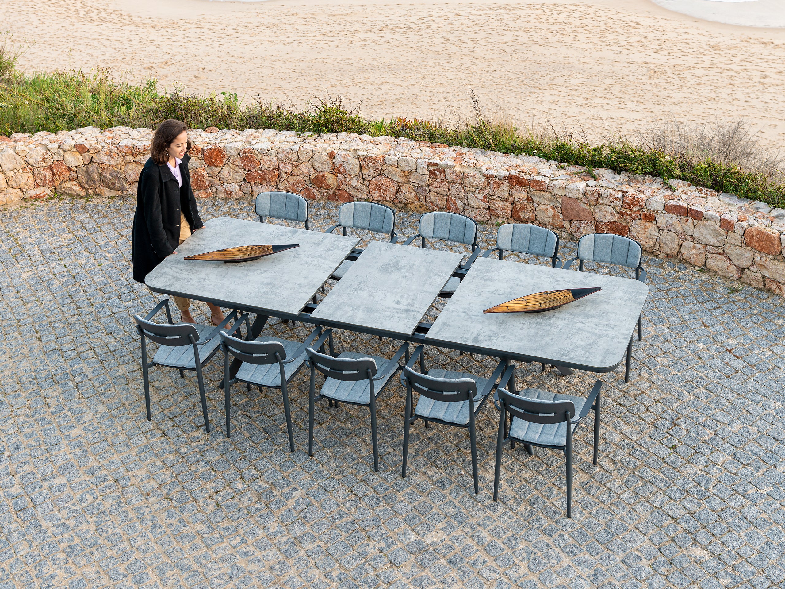 Outdoor Rimini dining table with a tempered glass top being extended by a woman pressing the mechanism and opening the table
