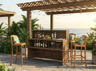 Outdoor bar setup with drinks and barware under a wooden pergola with ocean view.