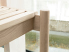Close-up of the detail of Trak indoor European light oak bench with modern rounded tubular legs